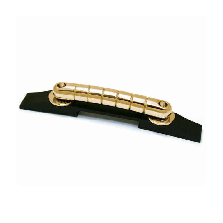 Gold-colored metal guitar bridge installed on a black wooden base shown on white background.