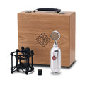 Silver bullet-shaped microphone with black shock mount, adapter, and wooden carrying case with logo.