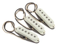 Three vintage white guitar pickups with black pole pieces and attached wires on a white background.