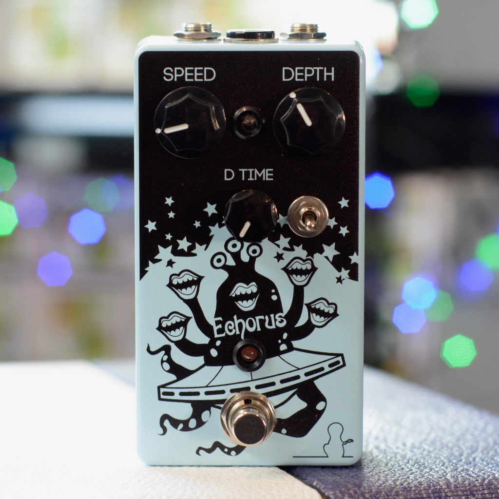 Front view of a light blue guitar effects pedal with knobs, toggle switch, footswitch, and graphic art on the faceplate.