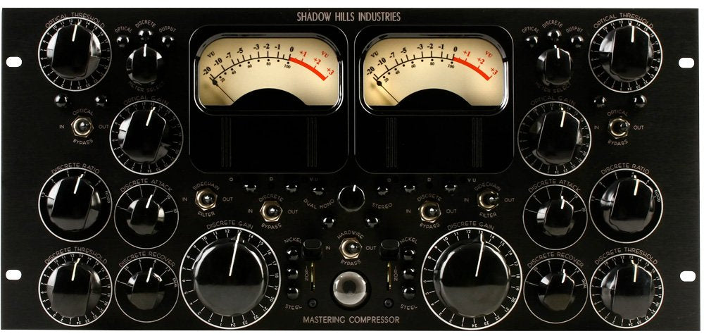 Front panel of a black audio mastering compressor with knobs, toggle switches, and dual VU meters.
