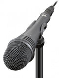 Black handheld microphone with visible metal grille, on/off switch, and attached audio cable on a stand.