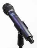 Handheld black microphone with a grille and visible button on a stand against a plain background.