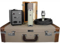 Microphone with power supply, cable, wooden storage box, and carrying case displayed on a surface.