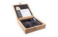 Open wooden box containing a microphone, foam windshield, clip, strap, and instruction manual.