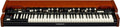 Keyboard synthesizer with two manuals, multiple control switches, and wooden side panels under a brown finish.