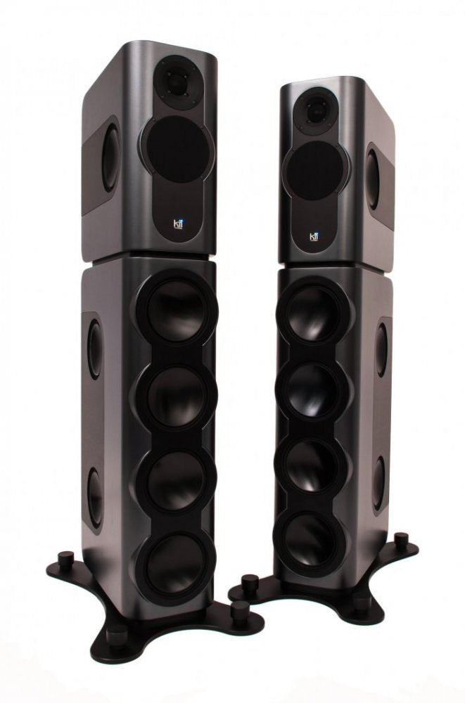 A tall, slim floor-standing Kii THREE BXT active loudspeaker column in a dark grey finish, formed by a compact Kii THREE monitor mounted on top of the taller BXT bass-extension module.