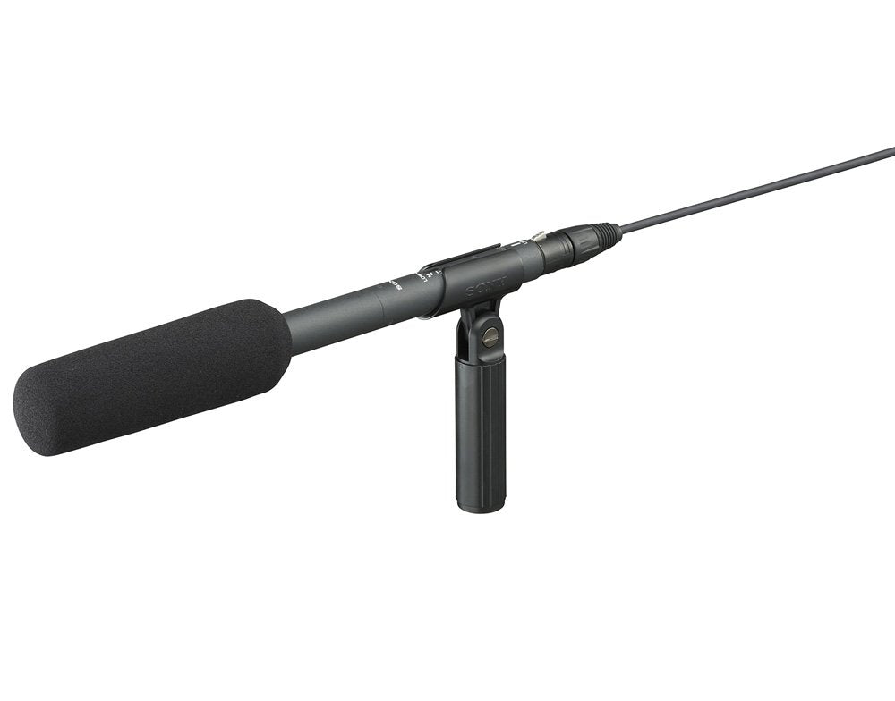 Black shotgun microphone with foam windscreen, cable, and attached handle mount on white background
