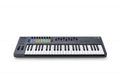 Black and white keyboard MIDI controller with 49 keys, multiple knobs, faders, colored pads, and a small display screen.
