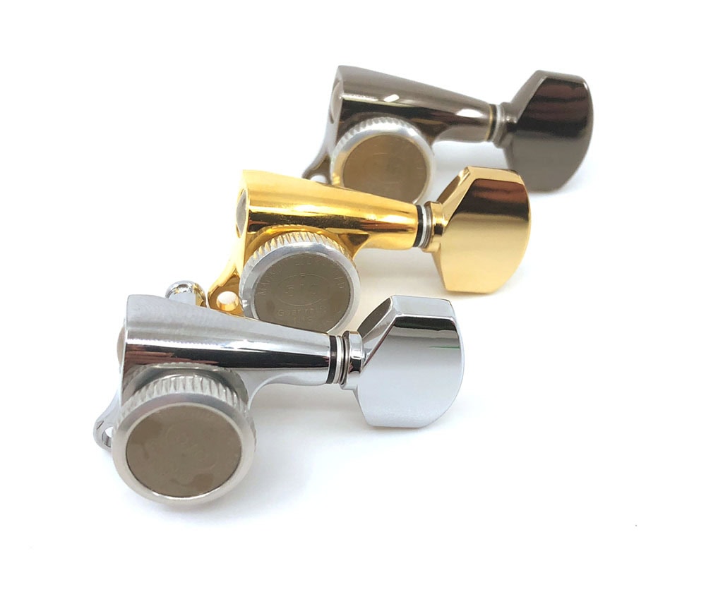 Three individual guitar tuning machine heads in silver, gold, and dark metallic finishes placed on a white background.