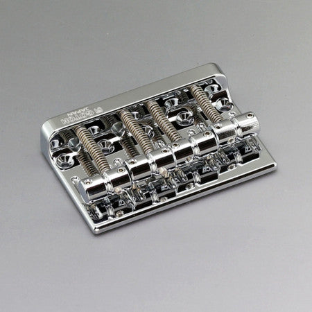 Silver metal bass bridge with four saddles and adjustment screws on a gray background.