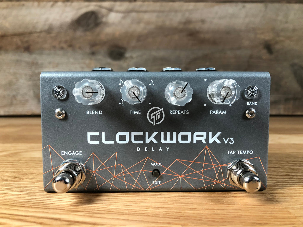 Gray Clockwork v3 delay pedal with four rotary knobs, two footswitches, and various control buttons on a wooden surface.