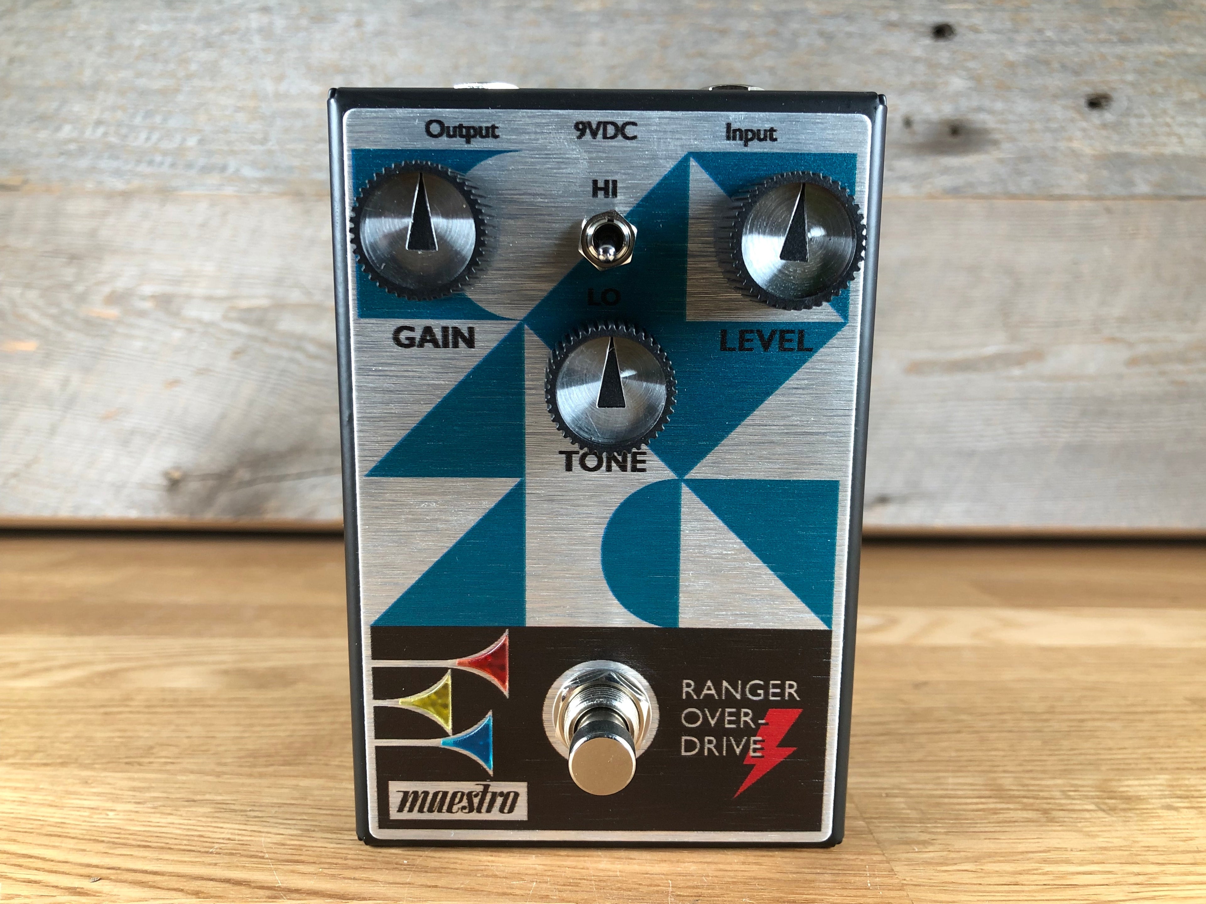 Silver and black guitar effects pedal with blue geometric design, three knobs, a toggle switch, and a footswitch.