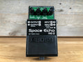 Black guitar effects pedal with multiple rotary knobs and labeled input/output jacks on top panel.