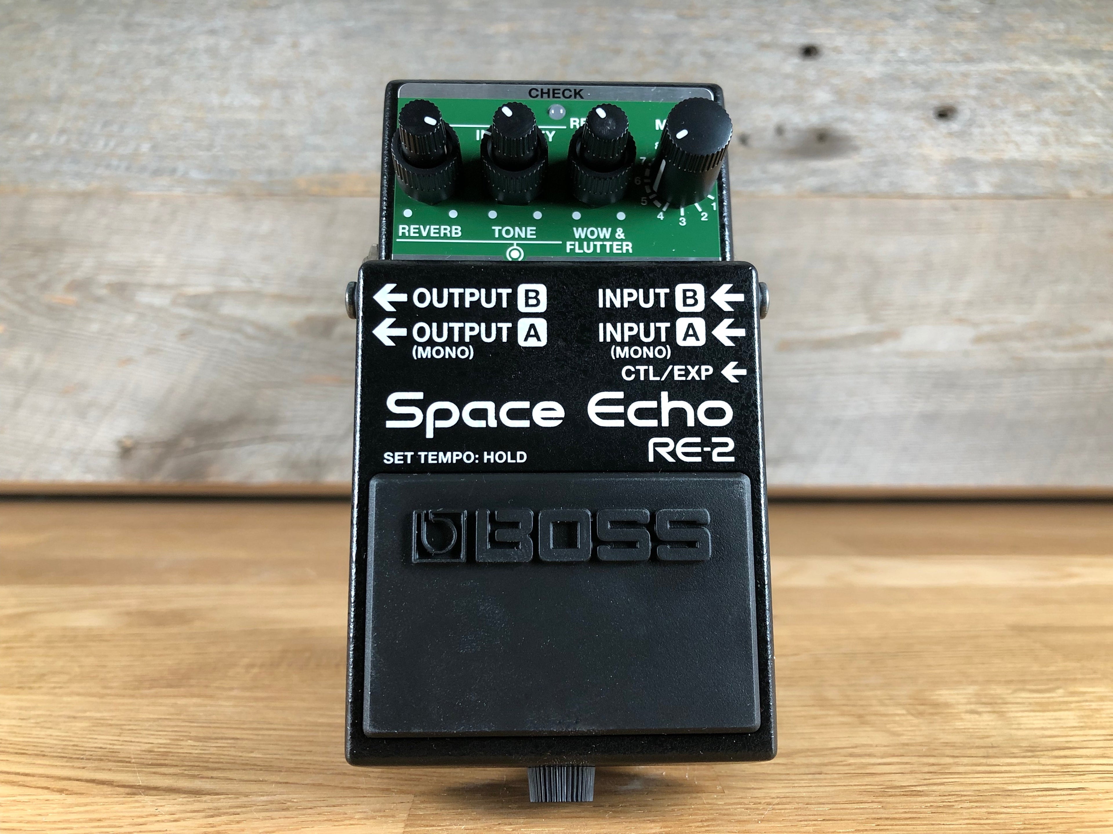Black guitar effects pedal with multiple rotary knobs and labeled input/output jacks on top panel.