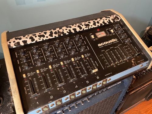 Black mixer/amplifier with six audio channels, multiple knobs and sliders, and several input connectors in front.
