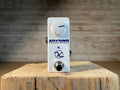White guitar effects pedal with one rotary knob, footswitch, and blue LED on wooden surface.