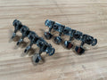 Two sets of four silver metal plate tuners with black screws lay on a wooden surface.