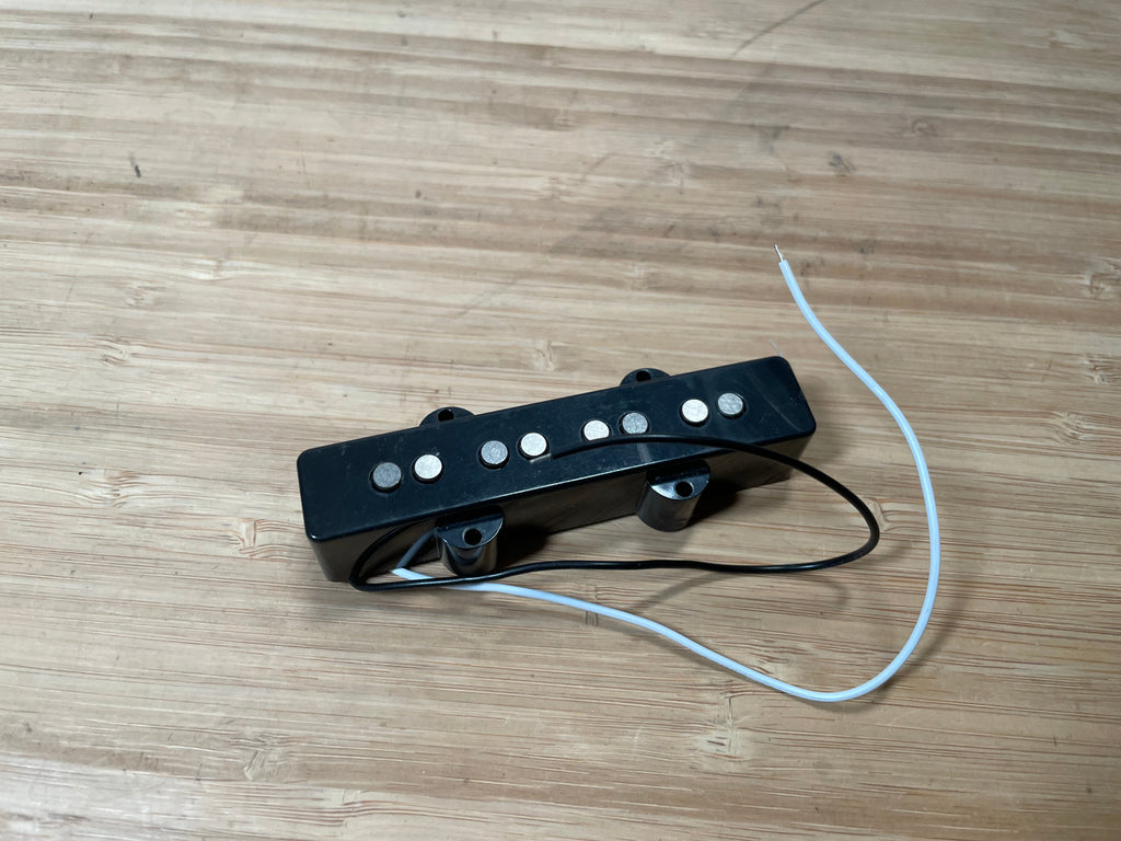 Black guitar pickup with pole pieces and two attached wires on wooden surface.