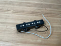 Black guitar pickup with pole pieces and two attached wires on wooden surface.