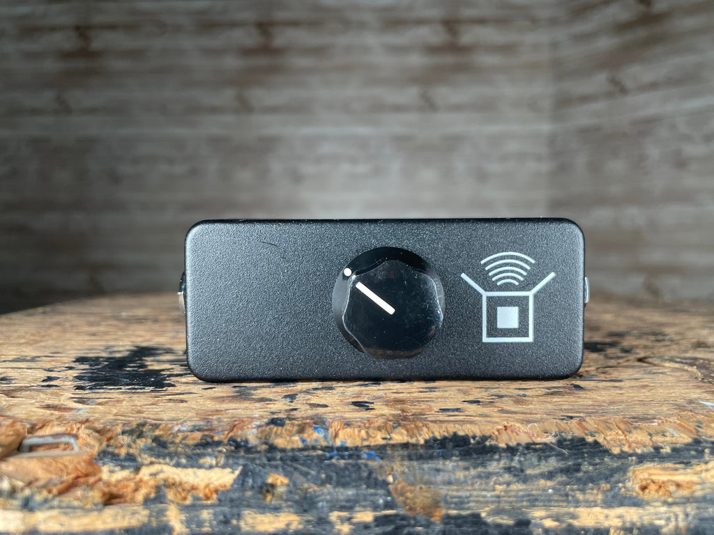 Small black rectangular pedal with a single black knob and a white icon on front panel.