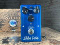 Blue guitar effects pedal with three knobs, a toggle switch, and a footswitch labeled Shiba Drive by Suhr.