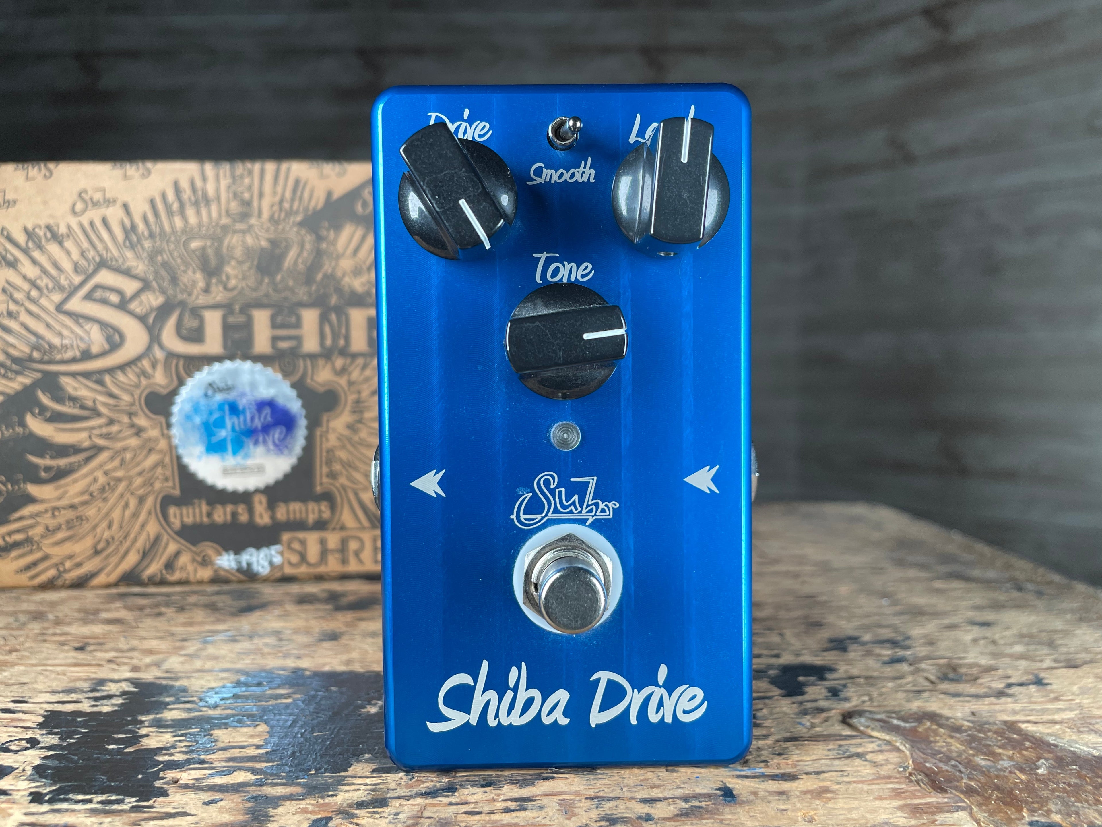Blue guitar effects pedal with three knobs, a toggle switch, and a footswitch labeled Shiba Drive by Suhr.