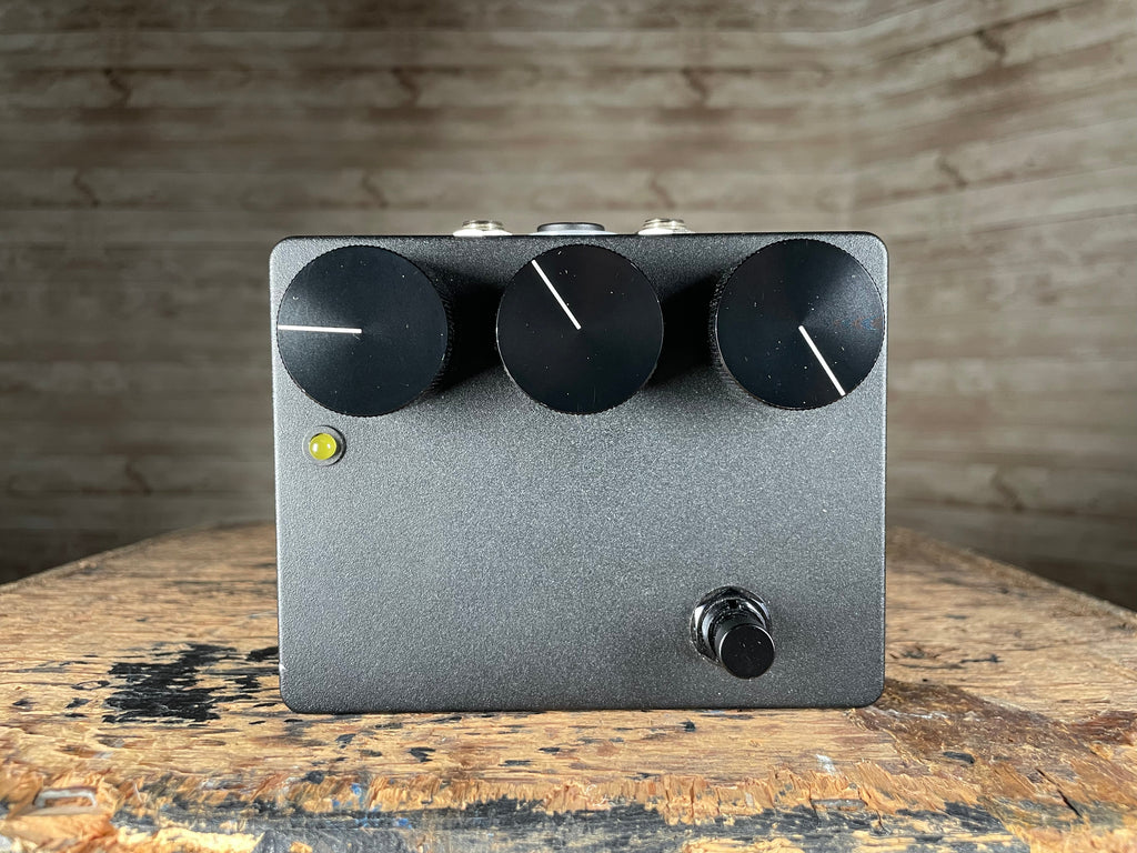 Black rectangular guitar effects pedal with three large knobs, one footswitch, and a yellow LED indicator on front panel.