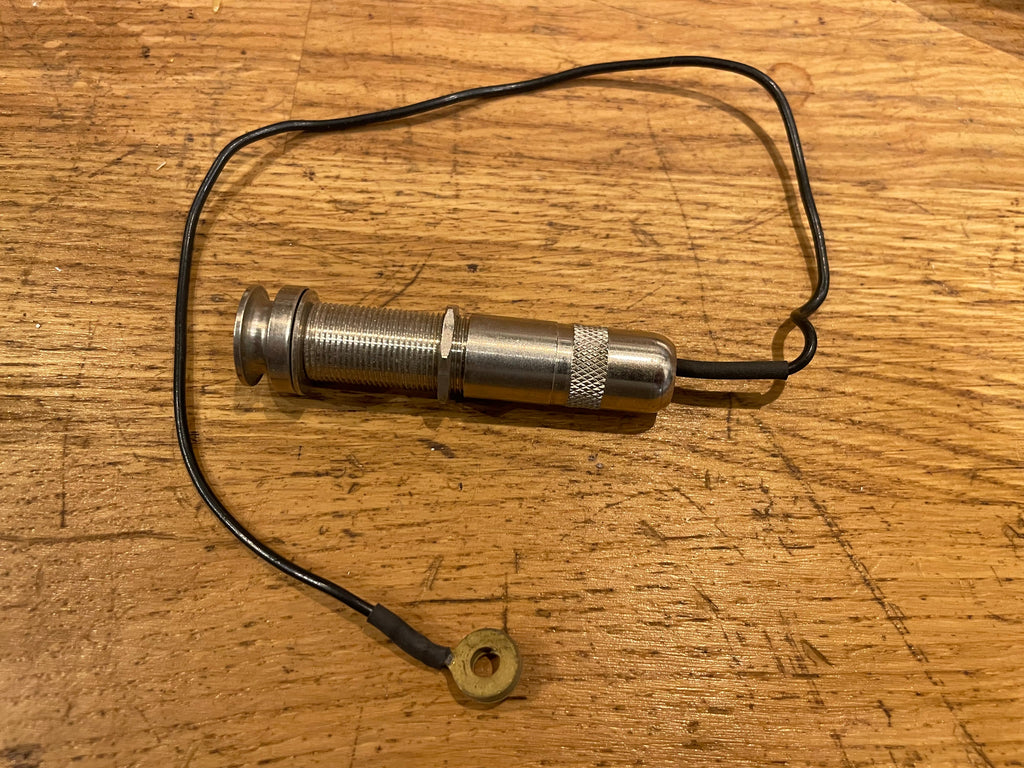 Metal passive pickup with threaded body and attached black wire ending in a brass ring terminal on wood surface.