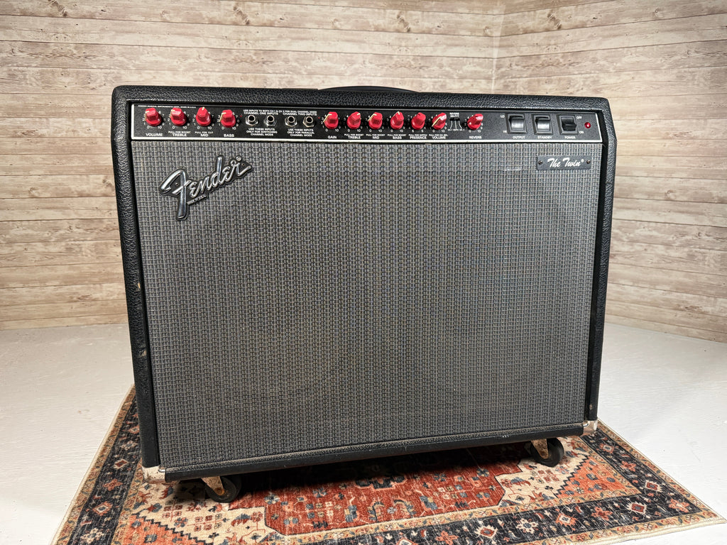 Black Fender amplifier with red control knobs and multiple input jacks on top panel, placed on casters.