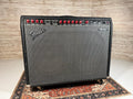 Black Fender amplifier with red control knobs and multiple input jacks on top panel, placed on casters.