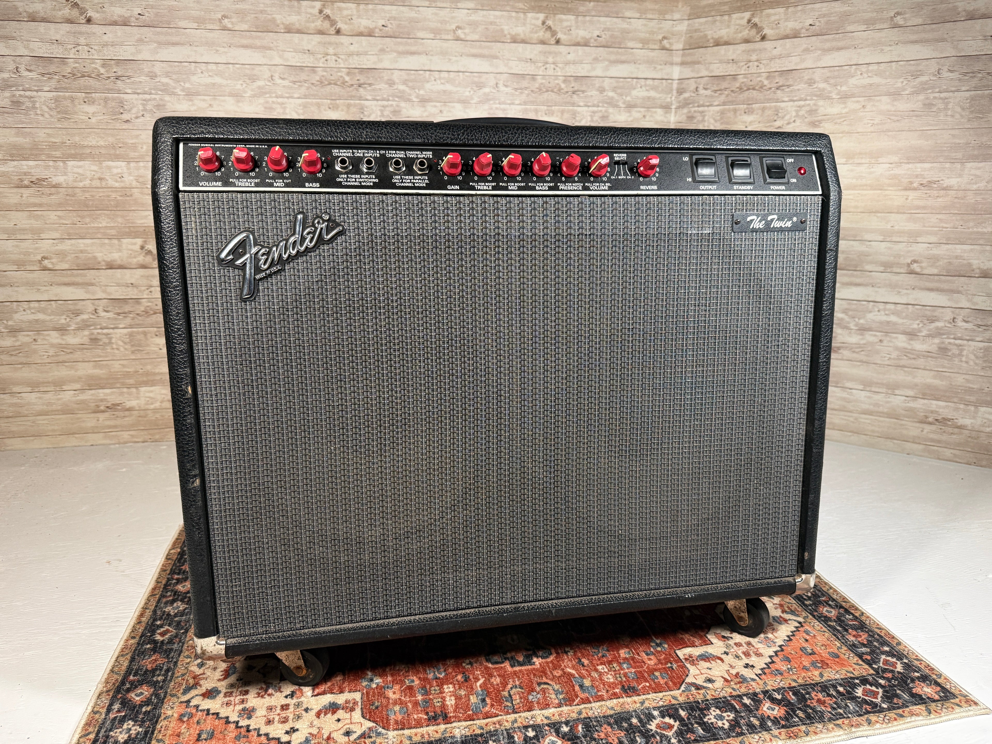 Black Fender amplifier with red control knobs and multiple input jacks on top panel, placed on casters.