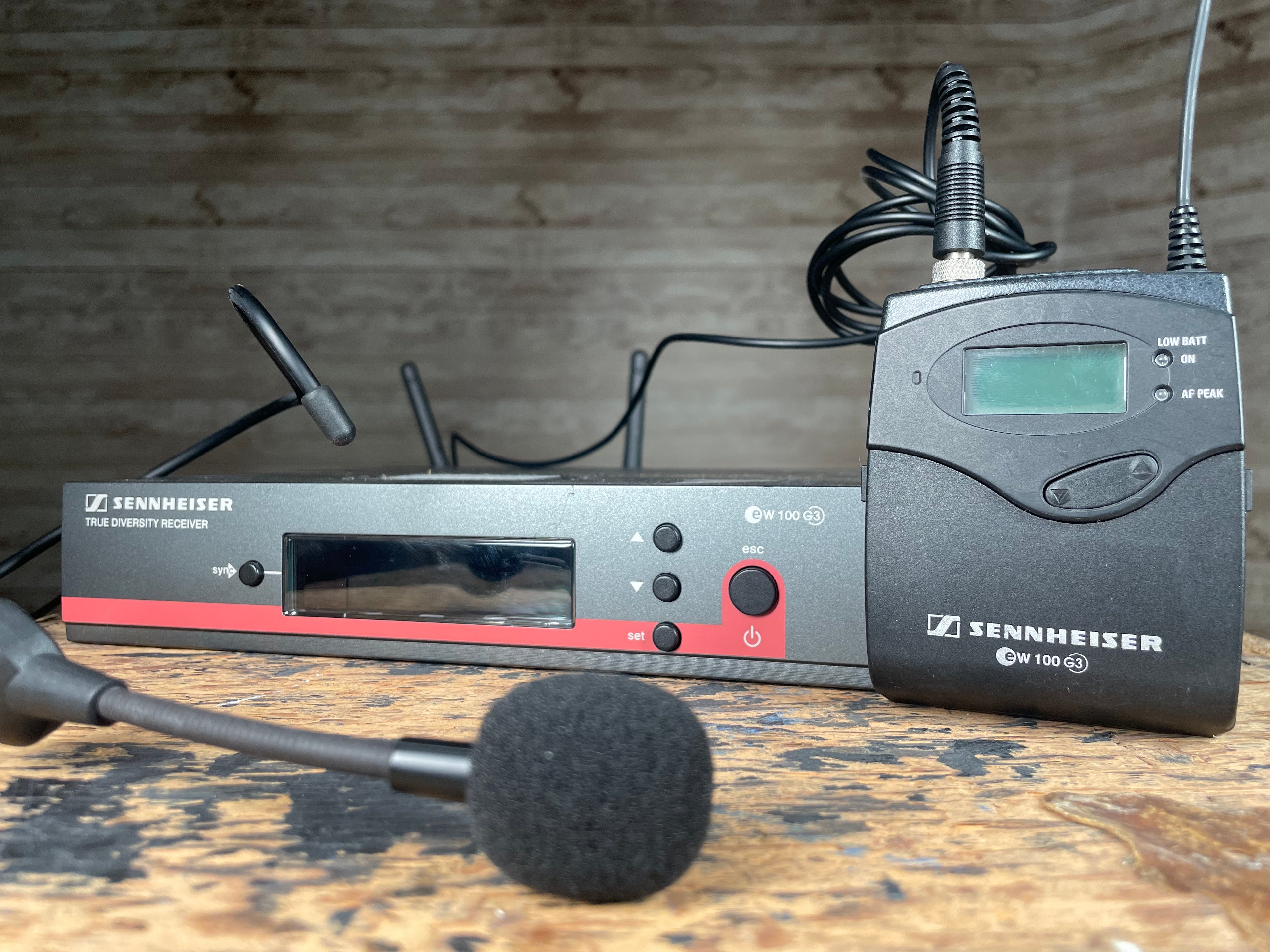Wireless receiver, bodypack transmitter, and headset microphone with foam windscreen on a wooden surface.