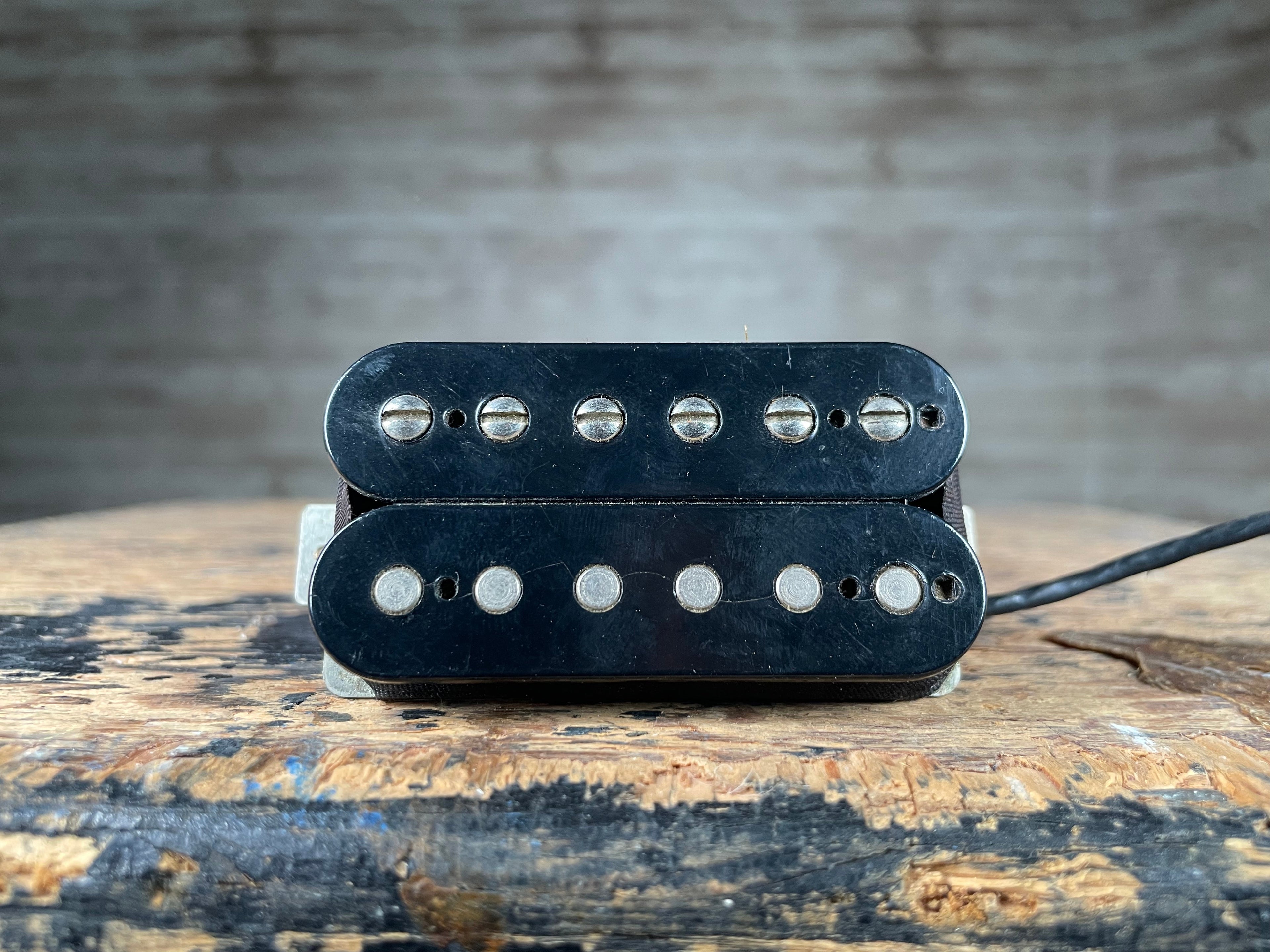 Black humbucker guitar pickup with six adjustable pole screws and attached wire on wooden surface.