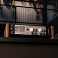 Two Notes Reload II audio device with wooden side panels and multiple rotary knobs and switches on the front panel.