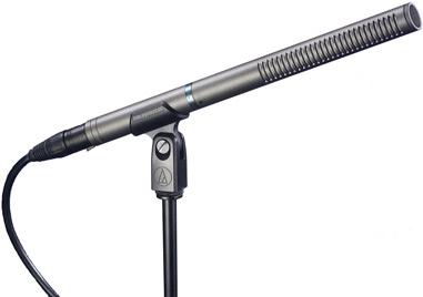 Black shotgun microphone on a stand with a cable connected via XLR connector and a rotary dial on the clip.