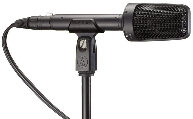 Black shotgun-style microphone mounted on a stand with attached XLR cable and low cut switch.