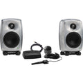 Pair of gray studio monitor speakers with black stands and accessories including microphone and sensor device laid out