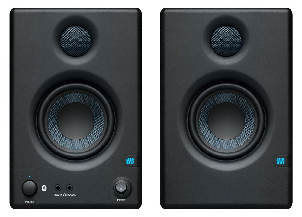 Two black studio monitor speakers with visible drivers, one has volume and power controls plus auxiliary and headphone jacks.