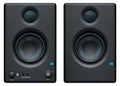 Two black studio monitor speakers with visible drivers, one has volume and power controls plus auxiliary and headphone jacks.