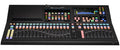 Black audio mixing console with multiple faders, knobs, colored buttons, and a screen showing audio levels and effects.