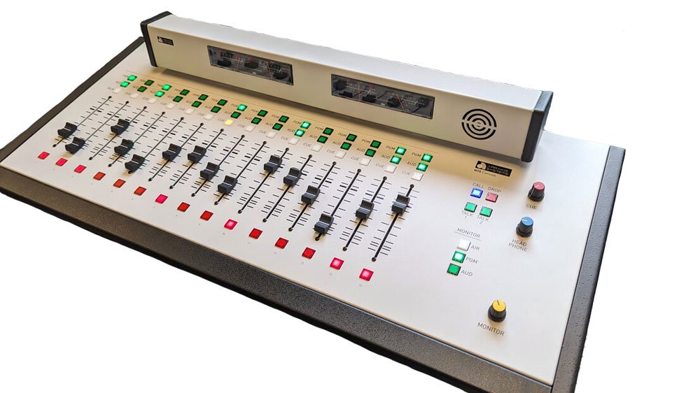 Audio mixing console with multiple sliders, buttons, knobs, meters, and indicator lights on a white panel.