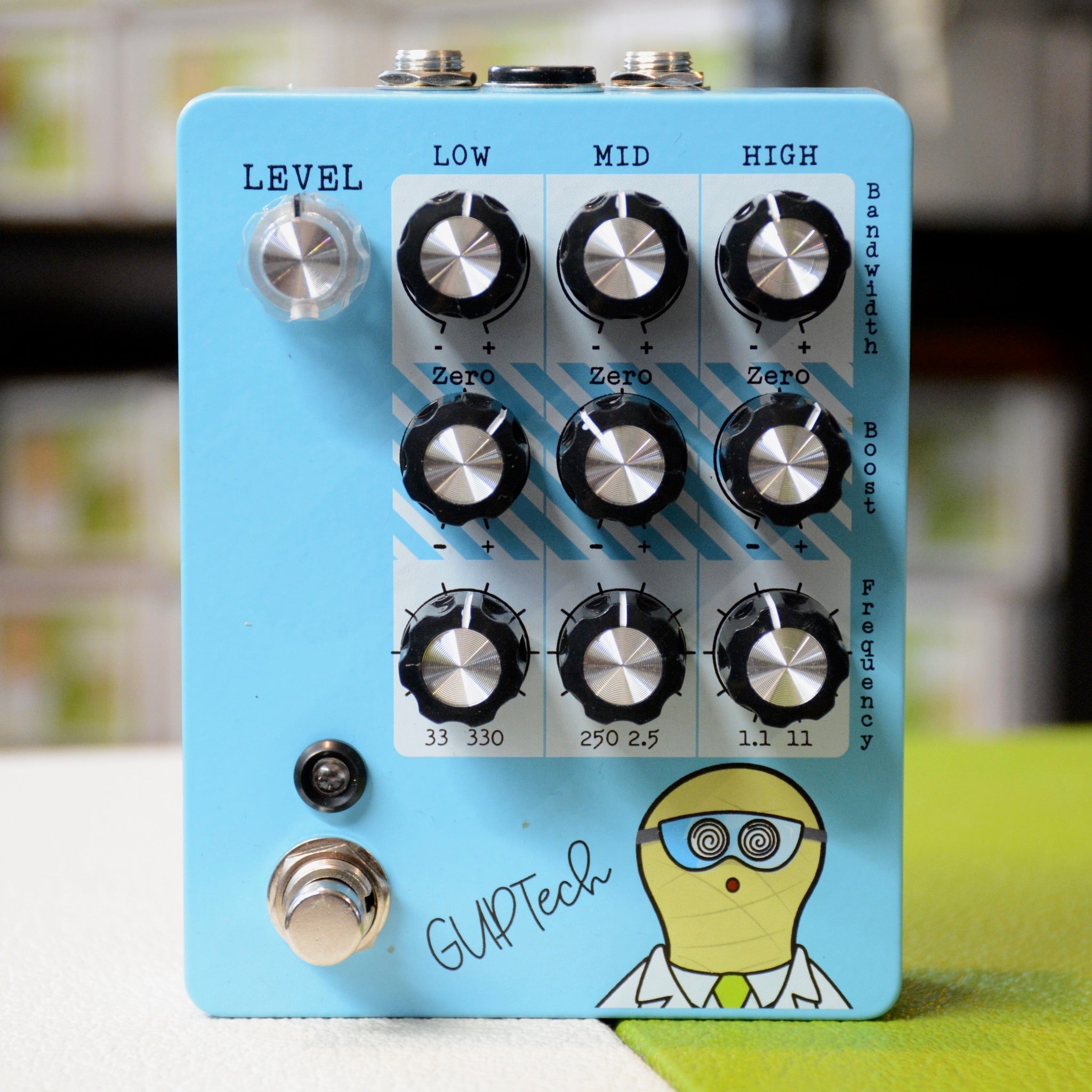Light blue audio effects pedal with multiple rotary knobs, a footswitch, a 1/4 inch jack, and cartoon scientist graphic.