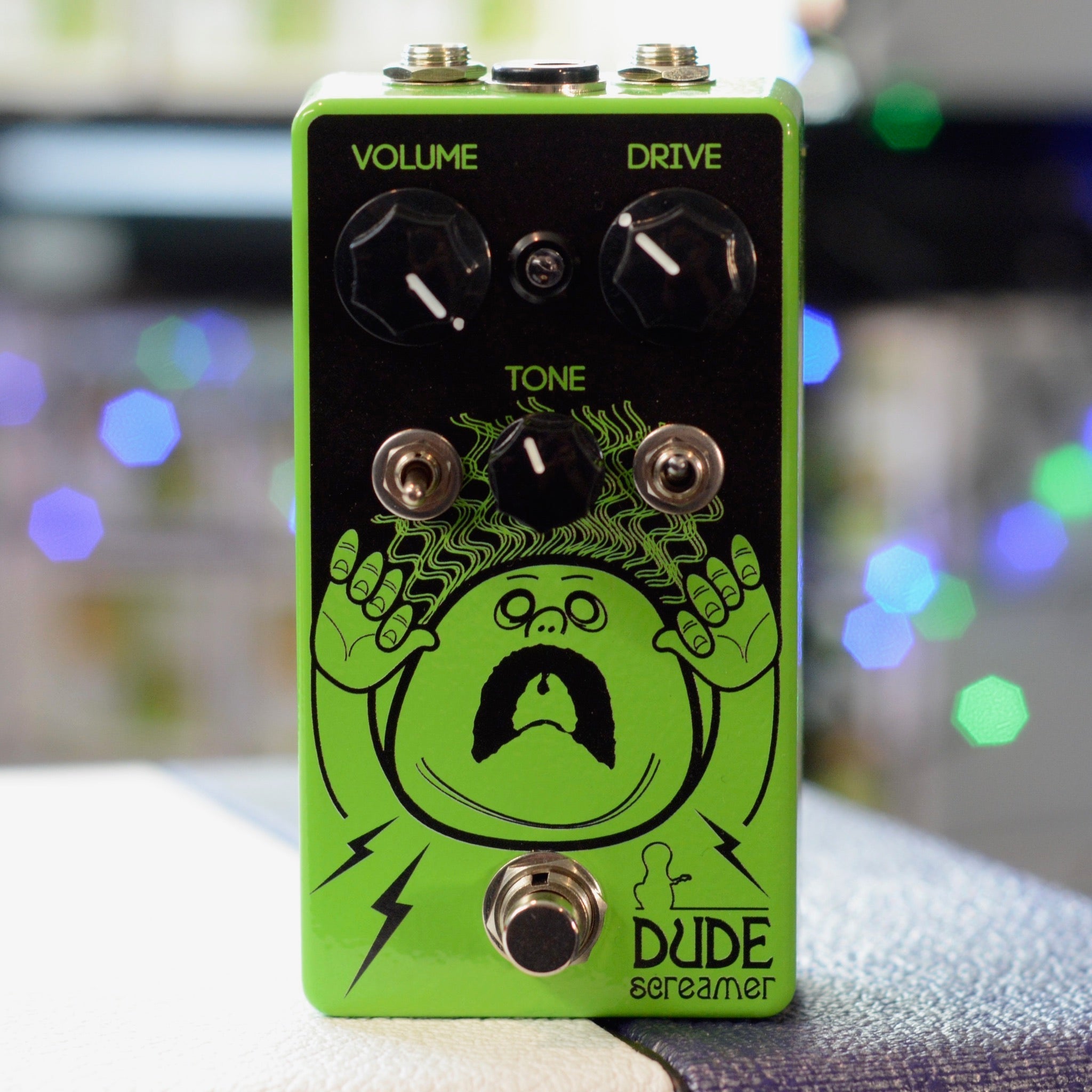 Green guitar effects pedal with three knobs, two toggle switches, one footswitch, and cartoon face artwork.