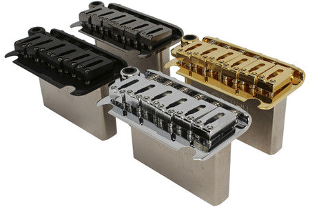 Three metal guitar bridge assemblies in black, silver, and gold finishes are shown side by side.