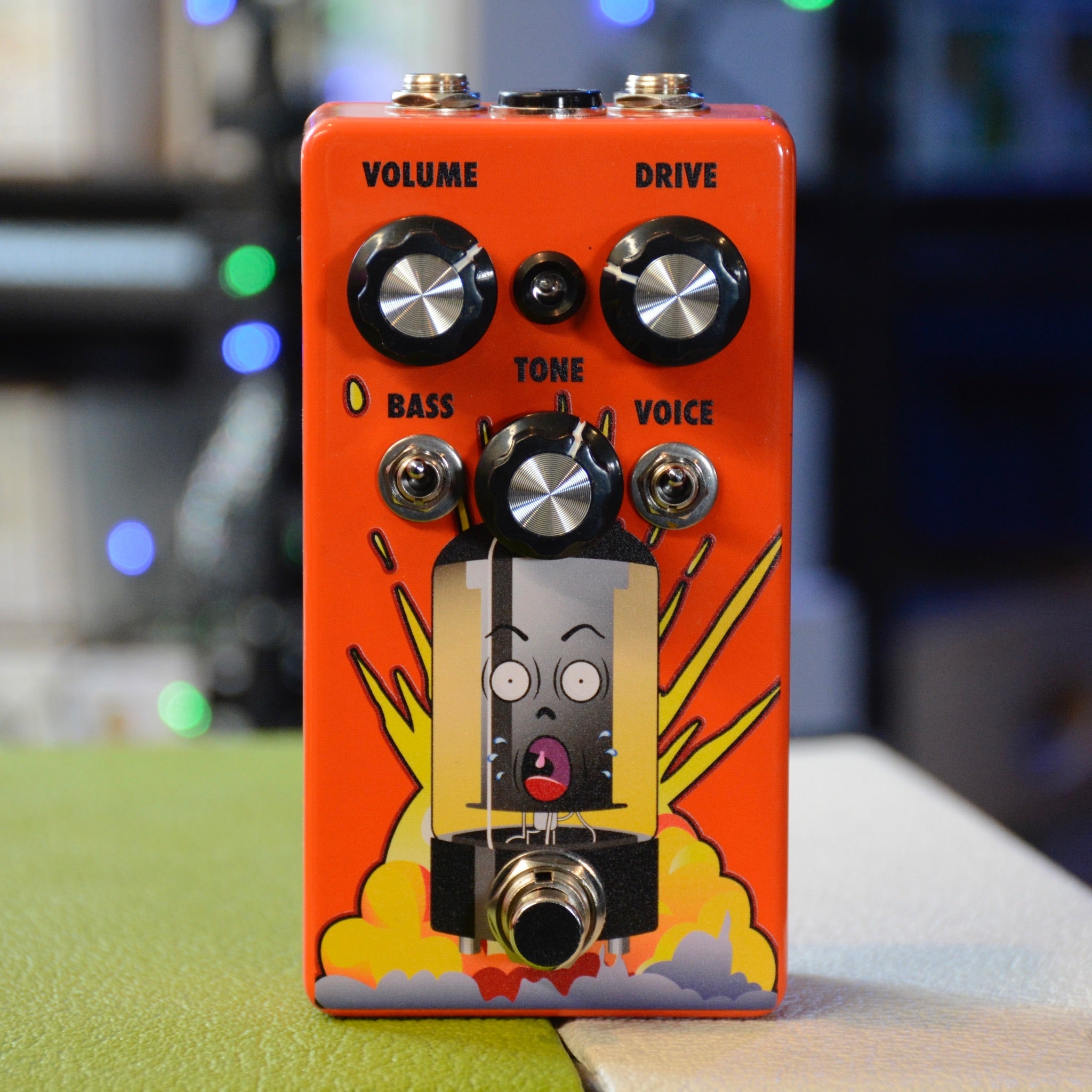 Orange guitar effects pedal with five control knobs, two toggle switches, and a footswitch featuring a cartoon vacuum tube graphic.