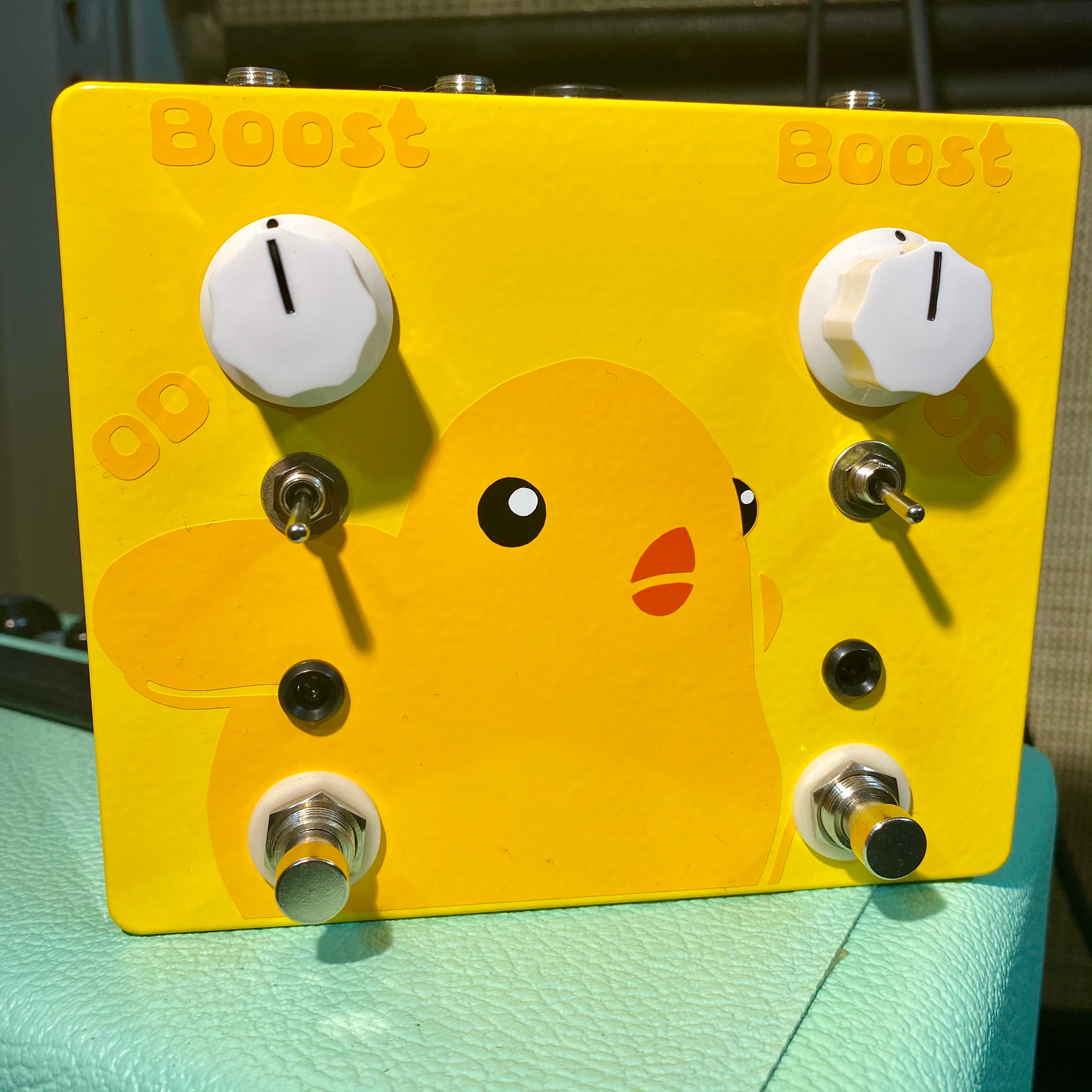 Yellow guitar effects pedal with duck graphic, two white knobs, two toggle switches, and two footswitches.