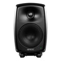 Front view of a black Genelec studio monitor speaker with a green LED light and protective mesh covers on drivers.