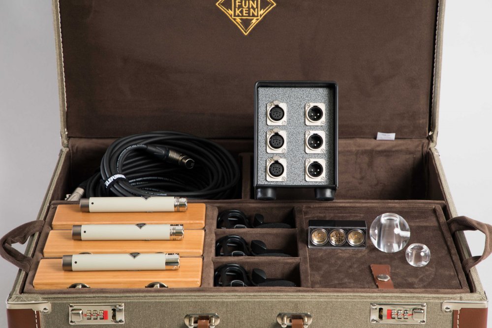 Open case containing three beige microphones, black box with connectors, clips, cable, and two clear spherical objects.