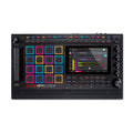 Top view of a black music production controller with colored pads, knobs, buttons, a touchscreen, and a speaker grille
